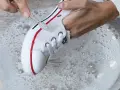 Manos limpian zapatillas de tela de color con cepillo en agua con jabón.