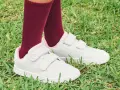 Niño con calcetines granates y zapatillas blancas con velcro, listas para limpiar y jugar en el césped.