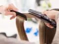 Manos peinando y alisando cabello con una plancha. ¡Sorprendentemente, se puede planchar la ropa con la plancha del pelo!