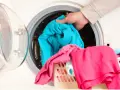 Mano cargando ropa azul en lavadora. Aprende como limpiar la lavadora para que tu ropa quede impecable.