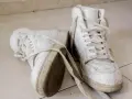 Par de zapatillas blancas sucias, con cordones desatados, sobre baldosas. Aprende como secar zapatillas blancas para que no se pongan amarillas.