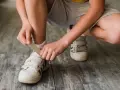 Niño se ata los cordones de sus zapatillas blancas. El número de pie según edad cambia rápido, ¡hay que estar al día!