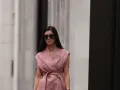 Mujer con gafas de sol y un elegante chaleco de lino rosa, atado a la cintura, pasea por la ciudad.