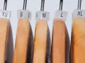 Perchas de madera con etiquetas de tallas XXS a XXL, mostrando la equivalencia talla europea y americana.