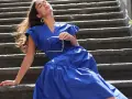 Mujer con vestido azul marino, gafas de sol en mano, sentada en escalones de piedra. Perfecta para combinar con zapatos para vestido azul marino.