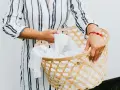 Manos sostienen una cesta de mimbre llena de ropa blanca, lista para lavar camiseta a mano.