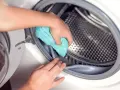 Mano limpiando la goma de la lavadora con un paño azul. Un paso esencial para saber como desinfectar una lavadora usada.