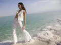 Mujer con traje blanco de encaje, posando en la orilla de un mar turquesa con formaciones de sal. Un look ibiza perfecto para el verano.