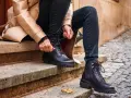 Persona se sienta en escalones de piedra, atándose unos pantalones anchos con botas militares negras.