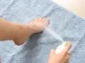 Persona rocía spray refrescante en sus pies cocidos sobre una toalla azul.