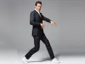 Hombre con traje a rayas y zapatillas deportivas blancas, en pose dinámica sobre fondo gris.