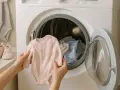 Manos sostienen un mameluco rosa para bebé, listo para meterlo en la lavadora. Aprende cómo lavar ropa de bebé fácilmente.