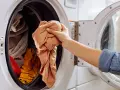 Mano saca ropa de lavadora. Es hora de limpiar lavadora a 90 grados para desinfectarla.