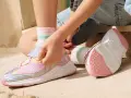 Niña ajustando sus zapatillas brillantes, talla 23 bebe, con detalles de arcoíris y calcetines a rayas.
