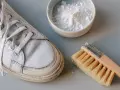 Un zapato de piel clara, un cepillo y un cuenco con polvo blanco, listo para aprender como limpiar zapatos de piel clara.