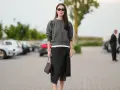 Mujer con falda satinada y zapatillas, bolso marrón y gafas de sol.