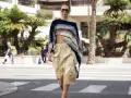 Mujer con un top corto de crochet y una falda vaporosa color beige, paseando por la calle con palmeras de fondo.
