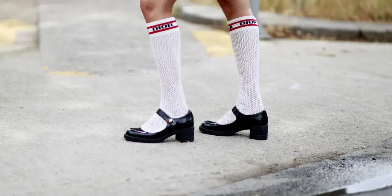Merceditas negras con calcetines blancos de rejilla y banda roja con logo "DIOR", un look infantil y chic.
