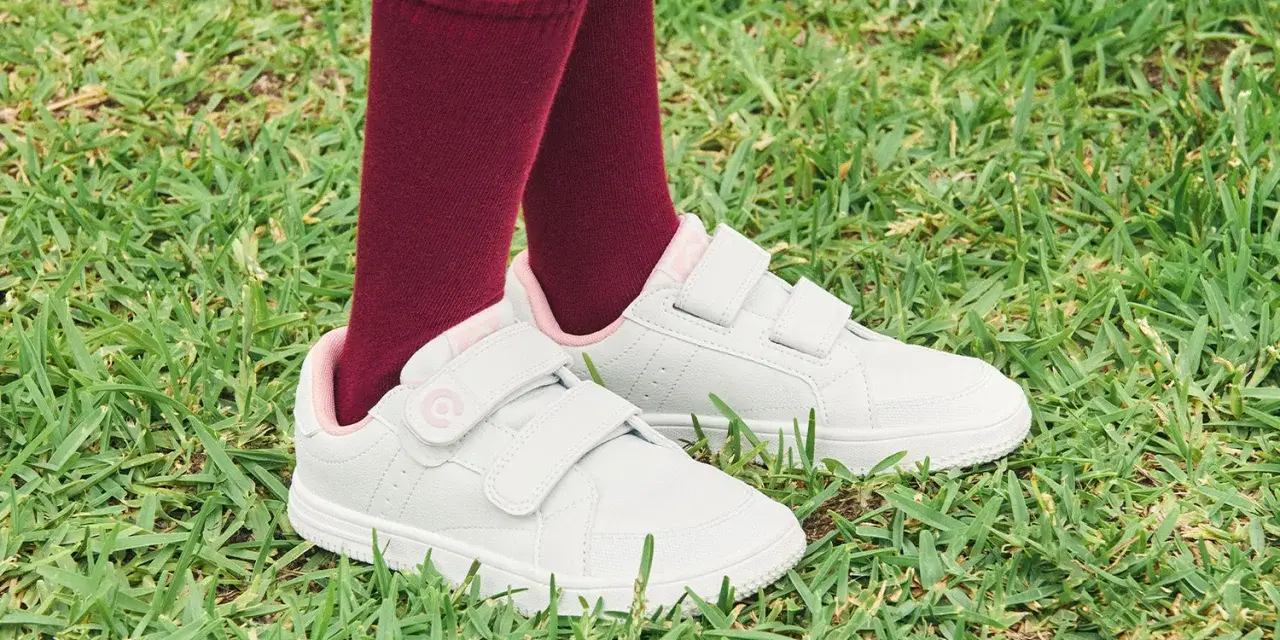 Niño con calcetines granates y zapatillas blancas con velcro, listas para limpiar y jugar en el césped.