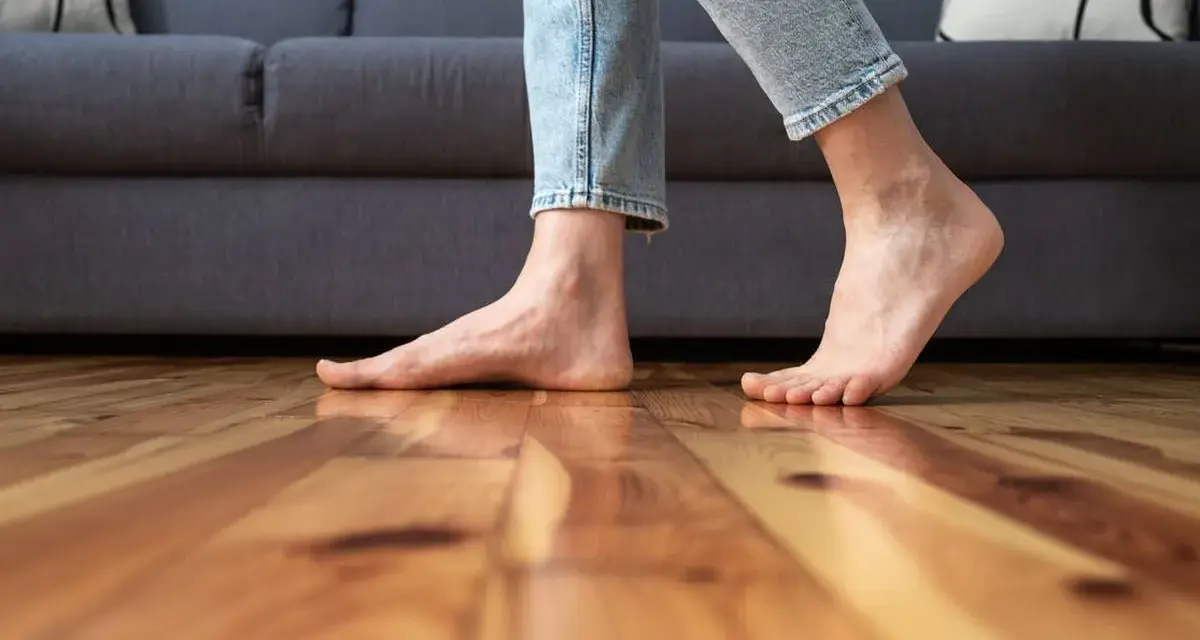 Pies descalzos sobre suelo de madera, sintiendo el frío al caminar cerca del sofá.