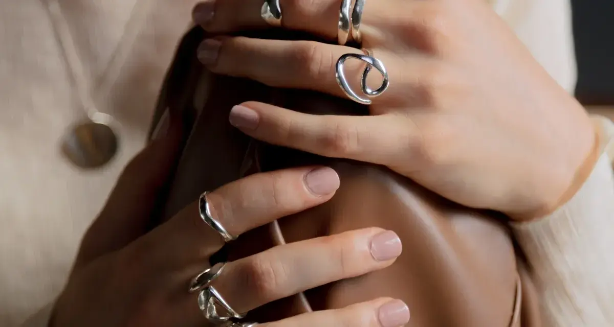 Manos adornadas con varios anillos de plata, uno de ellos con un diseño que recuerda a un anillo de flor.