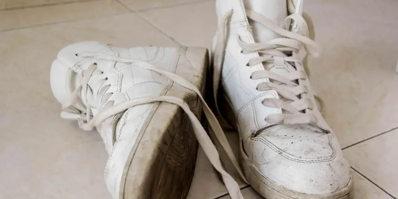 Par de zapatillas blancas sucias, con cordones desatados, sobre baldosas. Aprende como secar zapatillas blancas para que no se pongan amarillas.