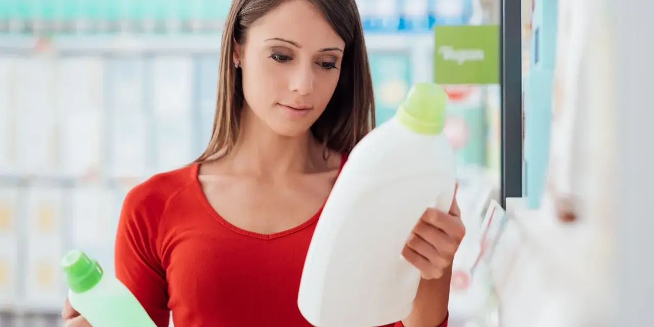 Mujer compara dos botellas de detergente, leyendo la etiqueta producto de limpieza.