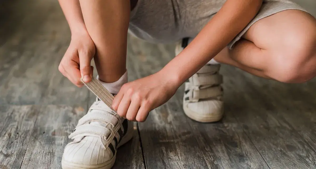 Niño se ata los cordones de sus zapatillas blancas. El número de pie según edad cambia rápido, ¡hay que estar al día!