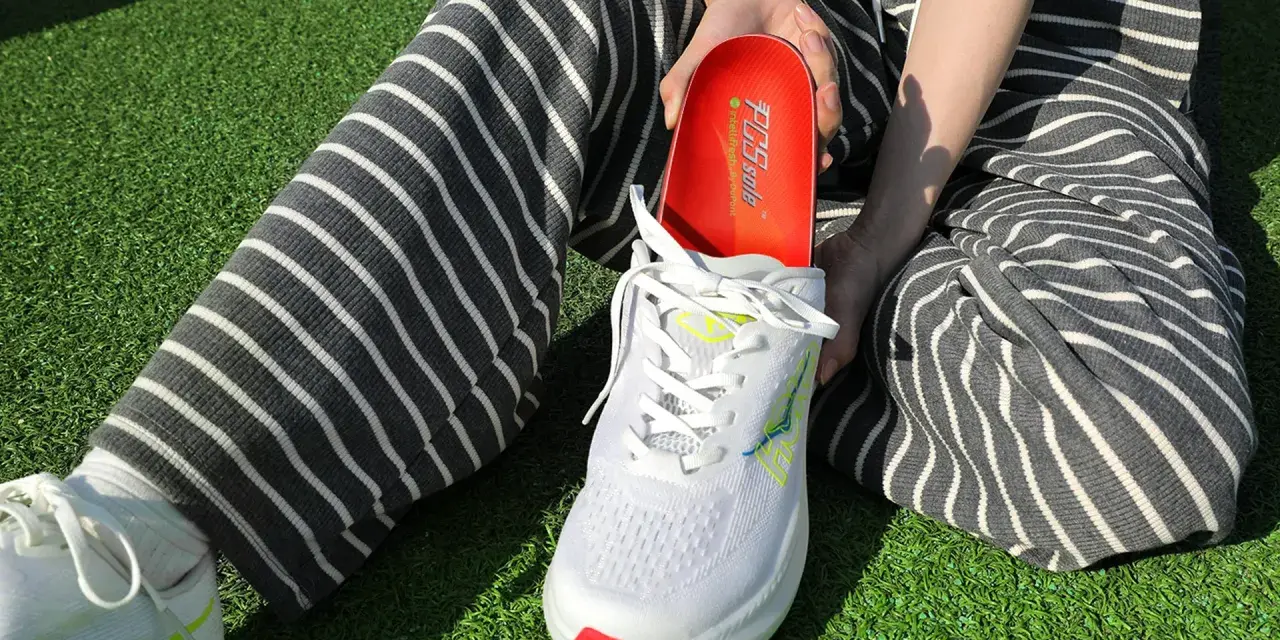Persona muestra una plantilla roja para el arco plantar, lista para ser colocada en un zapato deportivo blanco.