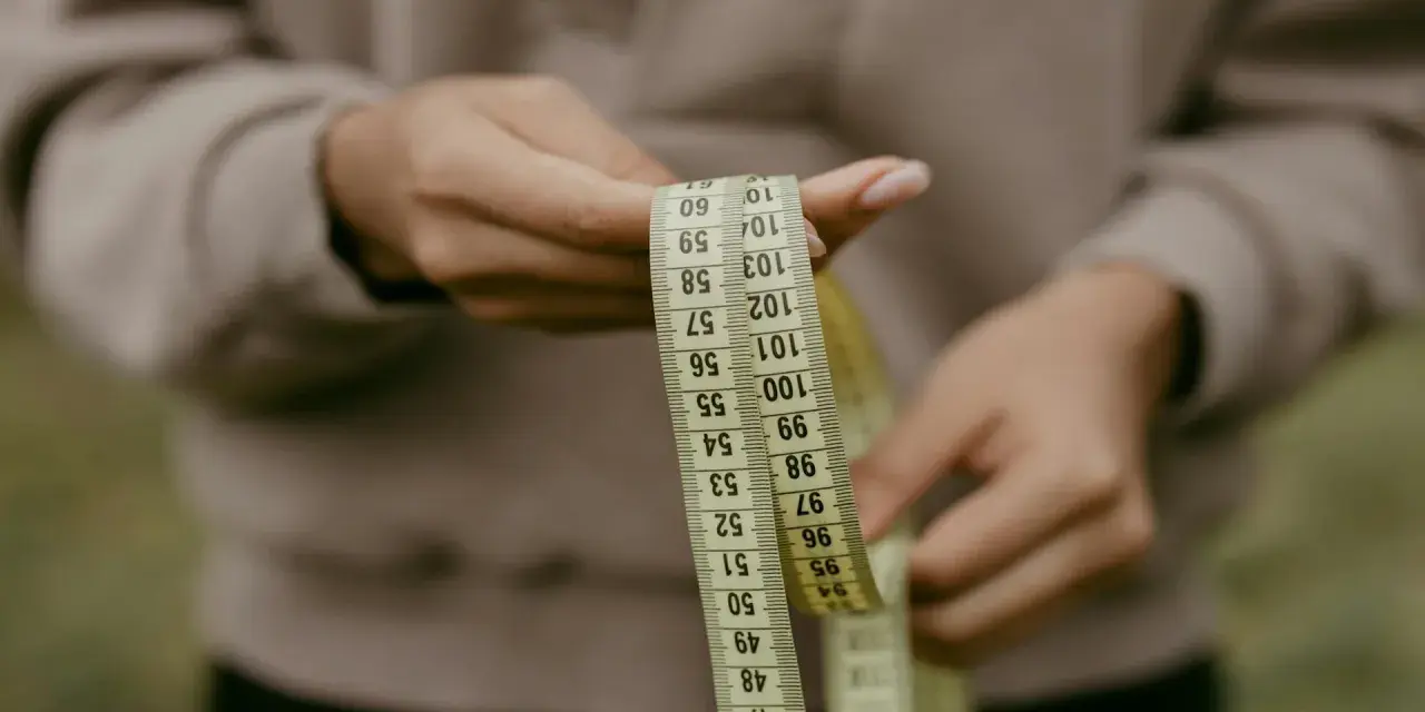 Manos sostienen cinta métrica. La talla 36 UK es un objetivo, pero la cinta muestra medidas en centímetros.