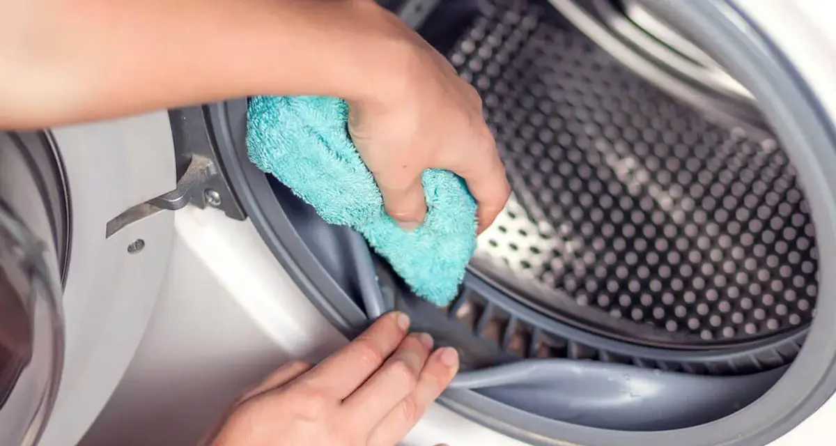 Mano limpiando la goma de la lavadora con un paño azul. Un paso esencial para saber como desinfectar una lavadora usada.