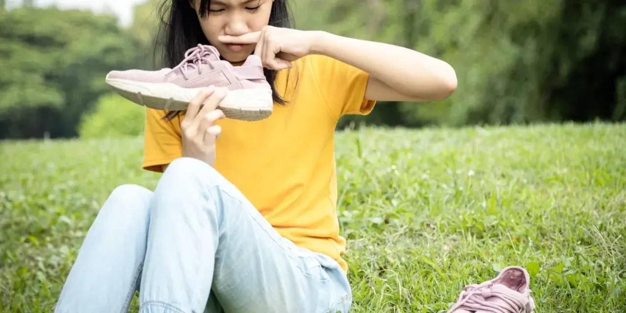 Niña con cara de asco huele un zapato, quizás por el sudor de los pies de niños tras un día de juegos.