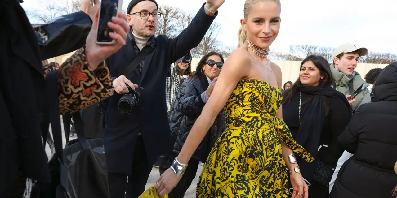 Mujer con un llamativo vestido globo amarillo y negro, rodeada de gente y fotógrafos.