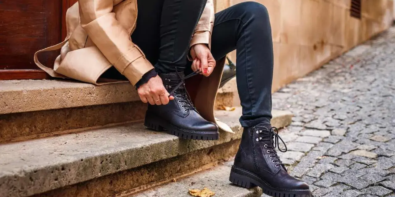 Persona se sienta en escalones de piedra, atándose unos pantalones anchos con botas militares negras.