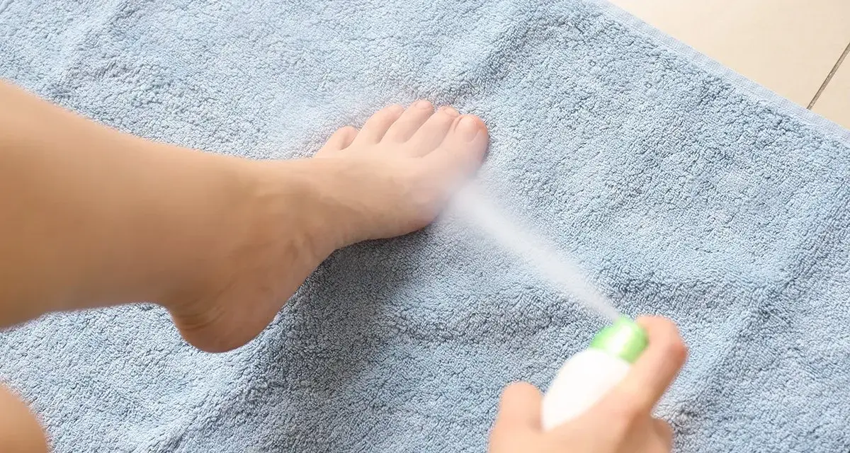 Persona rocía spray refrescante en sus pies cocidos sobre una toalla azul.
