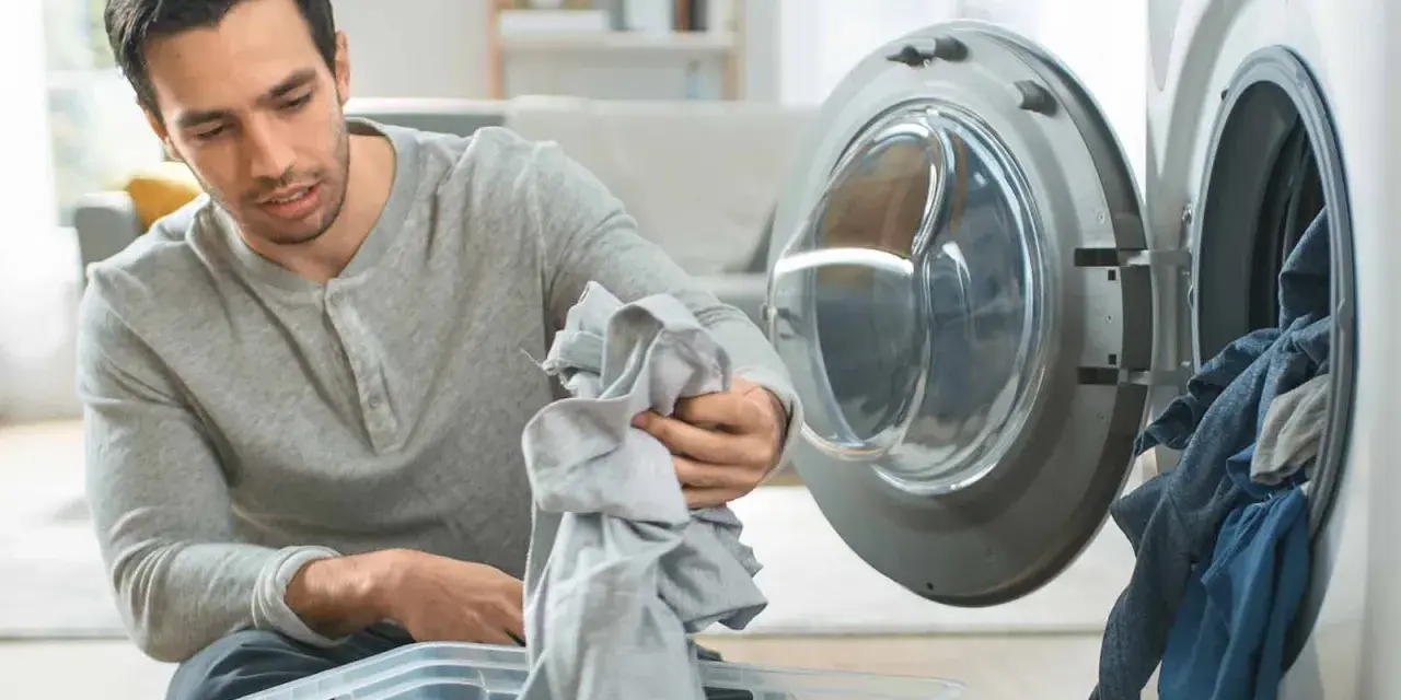 Hombre saca ropa de la lavadora, preocupado por la ropa que destiñe en la piel.