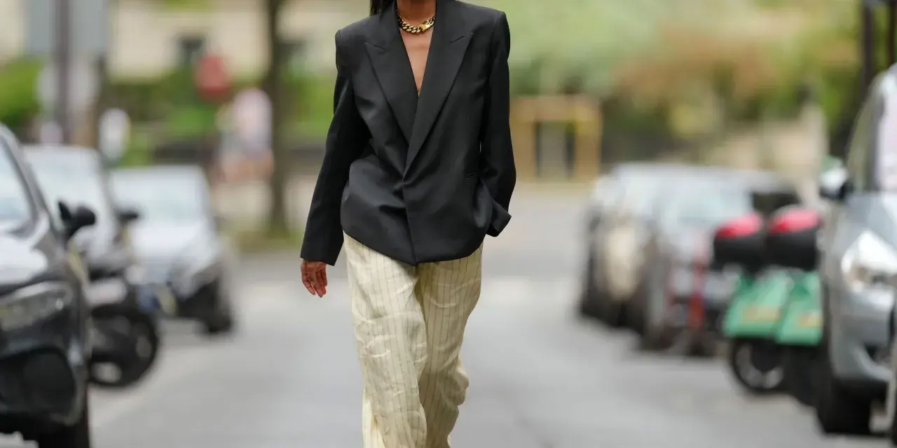 Mujer con blazer negro y pantalones de lino a rayas. Aprende como lavar pantalones de lino para mantenerlos impecables.