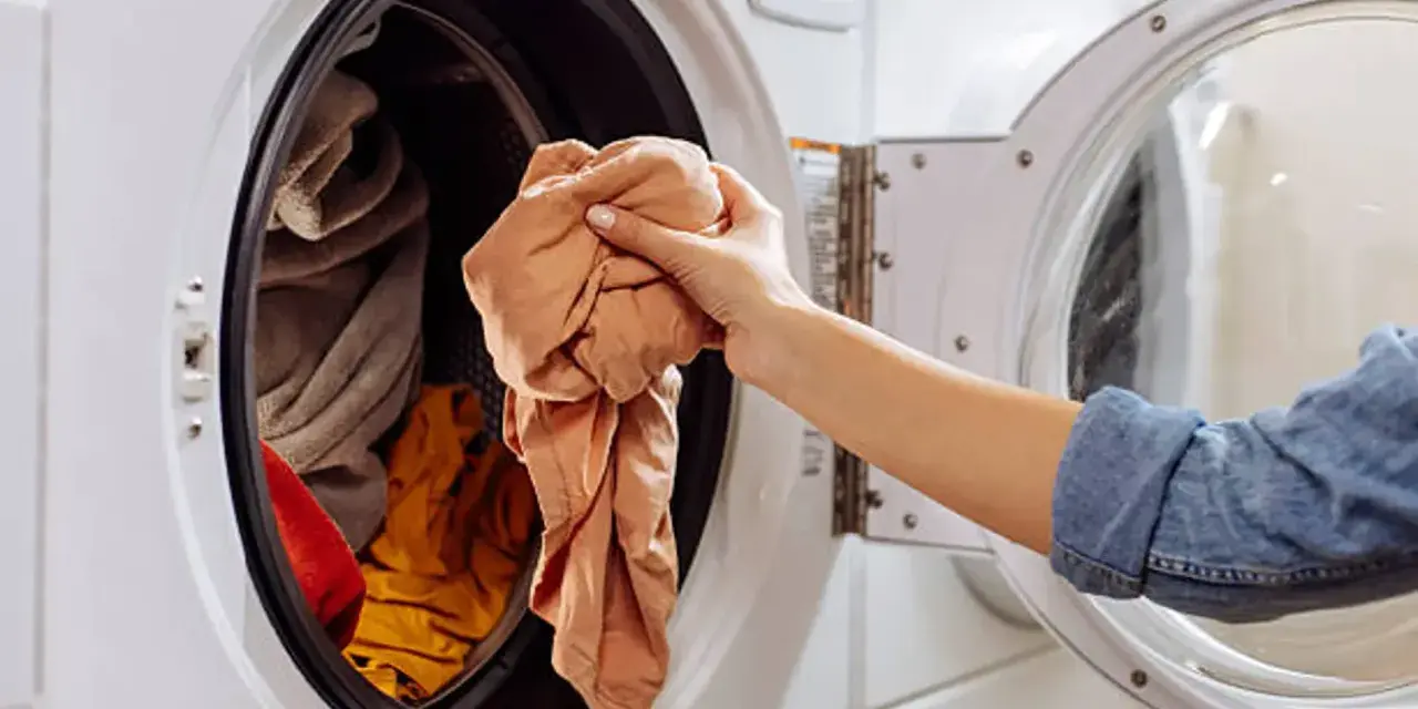 Mano saca ropa de lavadora. Es hora de limpiar lavadora a 90 grados para desinfectarla.