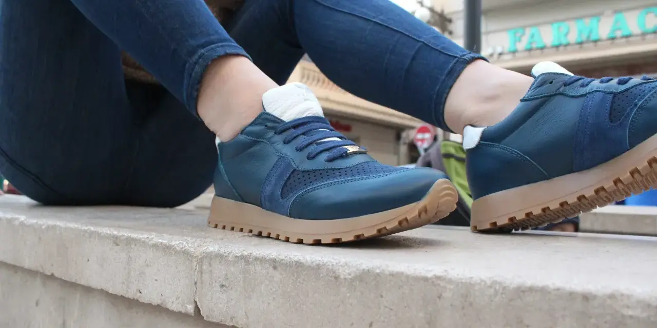 Un hombre luce unas zapatillas azules con cordones y suela de goma, combinadas con vaqueros oscuros.