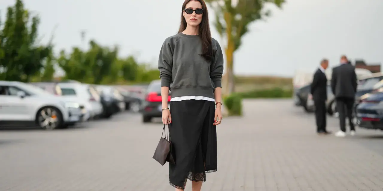 Mujer con falda satinada y zapatillas, bolso marrón y gafas de sol.