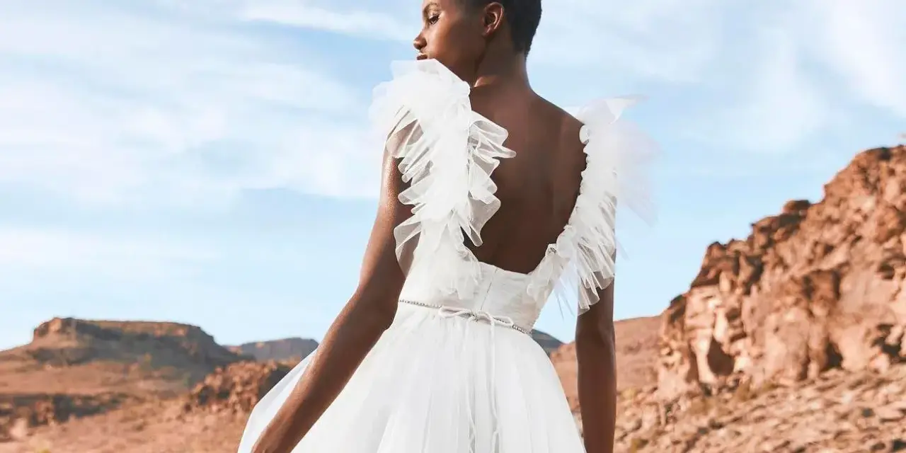 Novia con vestido blanco vaporoso, con volantes en los hombros, ideal para vestidos novia ibiza. Paisaje desértico al atardecer.