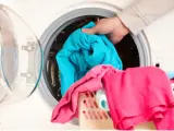 Mano cargando ropa azul en lavadora. Aprende como limpiar la lavadora para que tu ropa quede impecable.