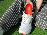 Persona muestra una plantilla roja para el arco plantar, lista para ser colocada en un zapato deportivo blanco.