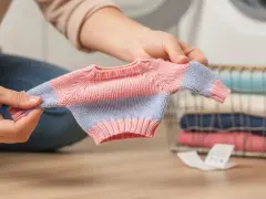 Manos sostienen un suéter diminuto, quizás para entender a qué temperatura encoge la ropa. Cerca, una cesta con ropa doblada.