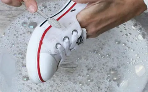Manos limpian zapatillas de tela de color con cepillo en agua con jabón.