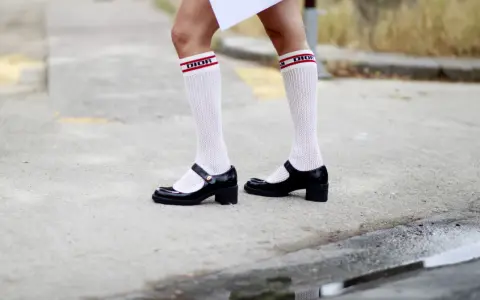 Merceditas negras con calcetines blancos de rejilla y banda roja con logo "DIOR", un look infantil y chic.