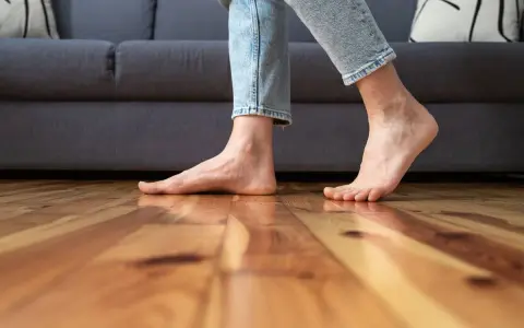 Pies descalzos sobre suelo de madera, sintiendo el frío al caminar cerca del sofá.