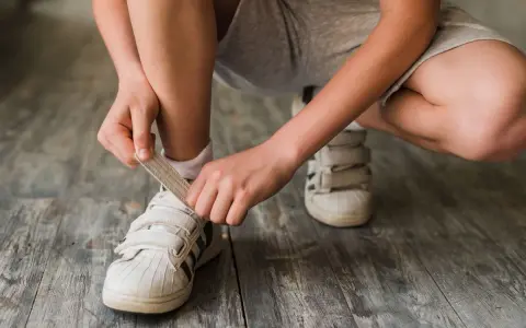 Niño se ata los cordones de sus zapatillas blancas. El número de pie según edad cambia rápido, ¡hay que estar al día!