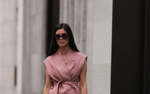 Mujer con gafas de sol y un elegante chaleco de lino rosa, atado a la cintura, pasea por la ciudad.