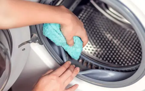 Mano limpiando la goma de la lavadora con un paño azul. Un paso esencial para saber como desinfectar una lavadora usada.